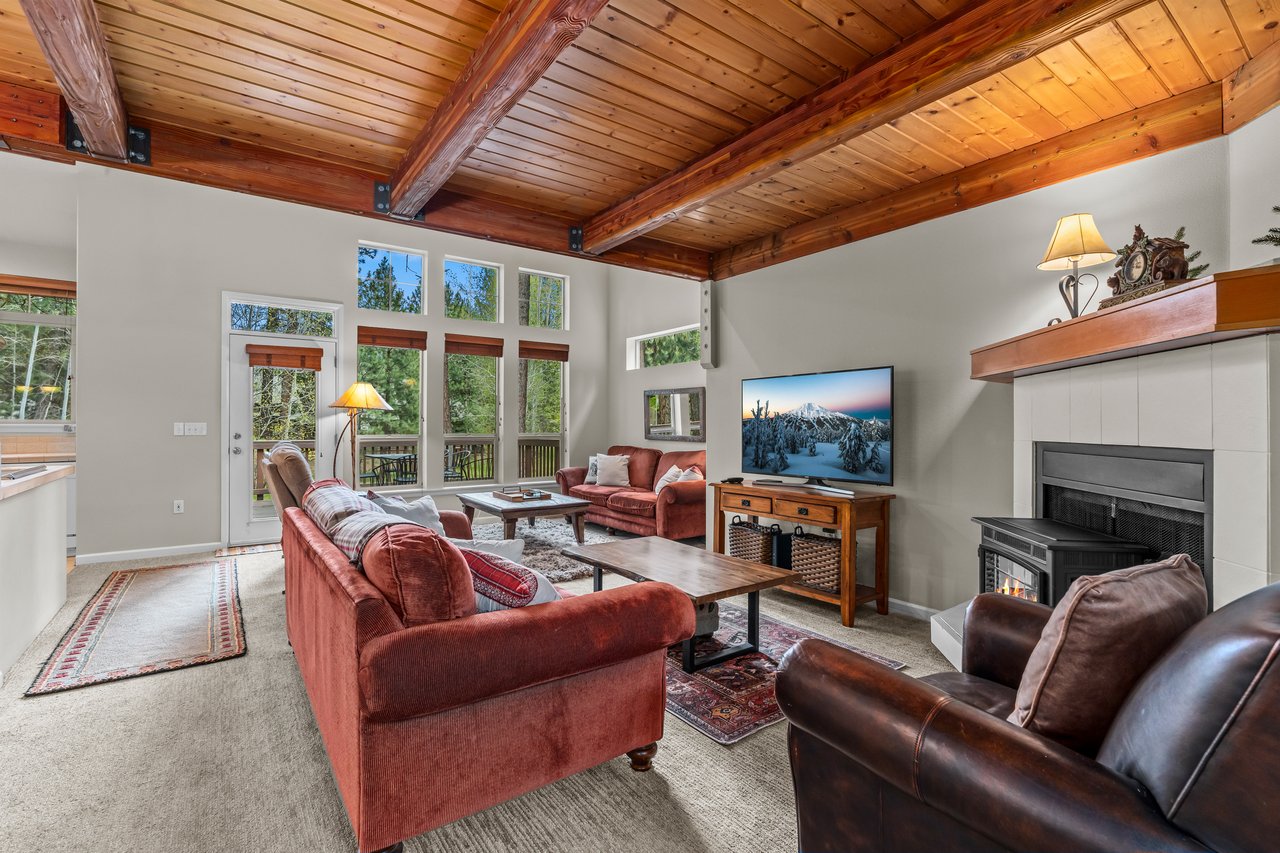Gather under soaring wood beam ceilings in your inviting living room, where plush seating faces a cozy fireplace and mountain views await just beyond tall windows.