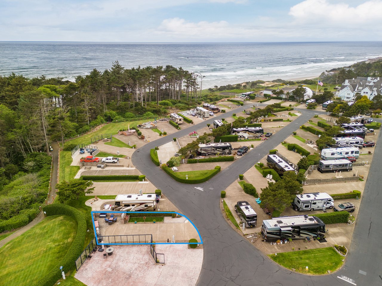 Aerial view of a coastal RV resort featuring spacious sites surrounded by lush greenery, with the Pacific Ocean and sandy beach visible in the background.