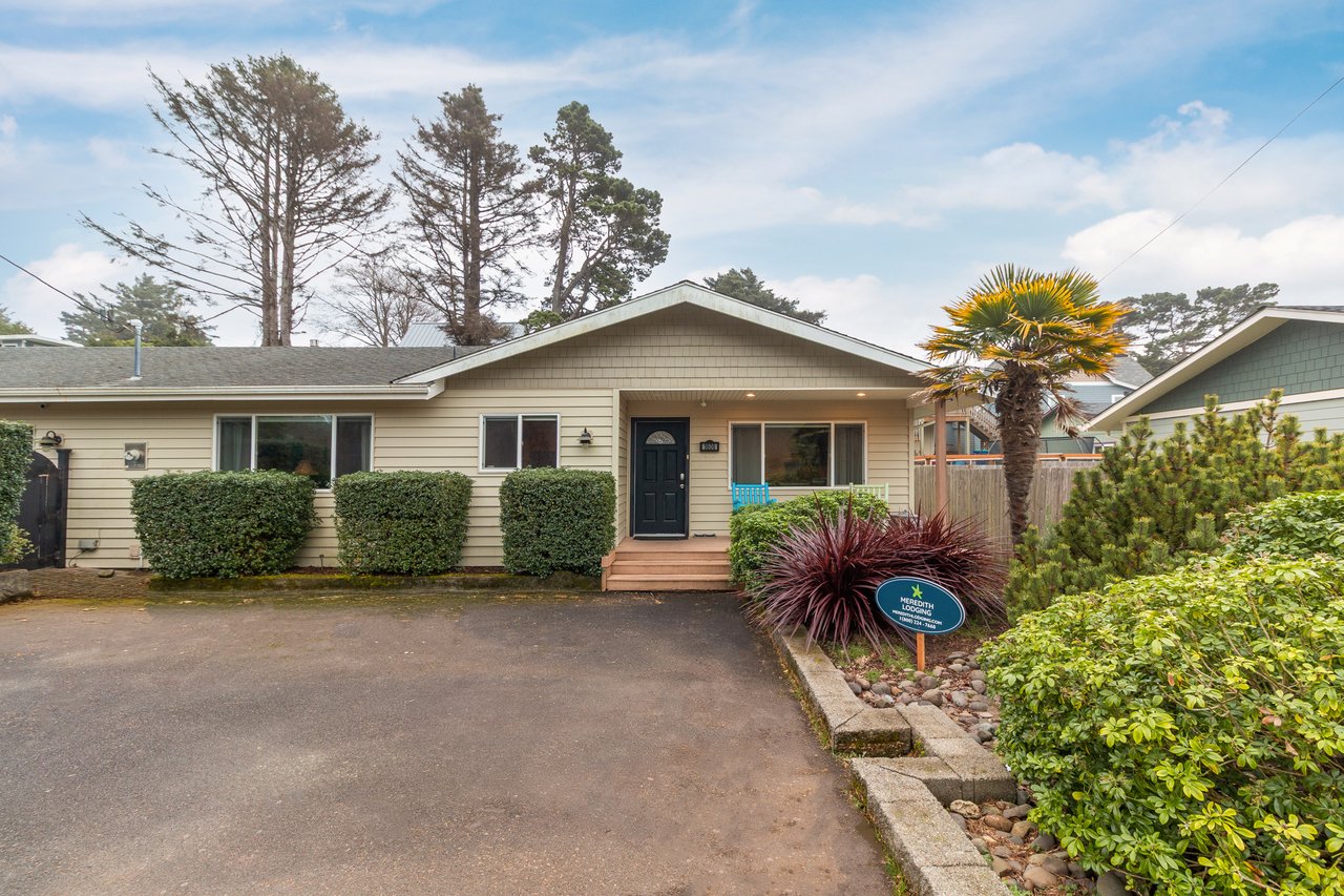 Charming coastal cottage with manicured landscaping and mature trees creates a welcoming arrival experience in this peaceful neighborhood setting.