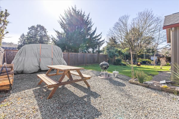 Your private backyard oasis awaits with a picnic table, BBQ grill, and spacious lawn surrounded by mature trees.