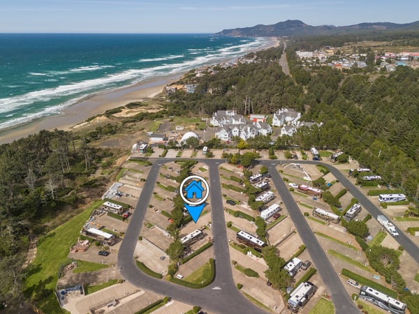 Aerial view of coastal vacation rental community nestled between pristine beach and forested hills, with oceanfront access and mountain backdrop.