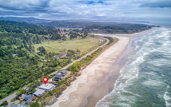 Aerial view showcasing the property's prime coastal location along sandy shores, with forested hills and ocean vistas defining the surrounding landscape.