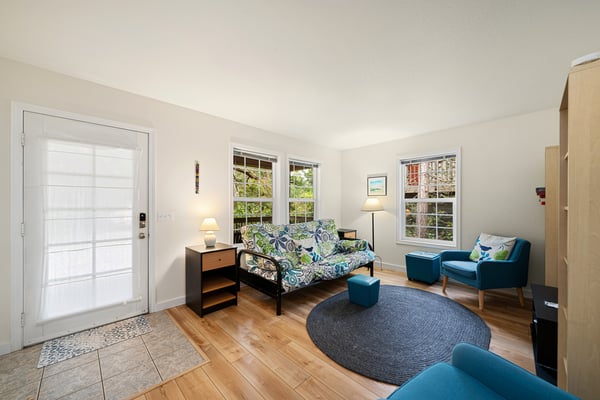 Settle into this bright, airy living room with comfortable seating, warm wood floors, and garden views streaming through three windows. Your peaceful retreat awaits.