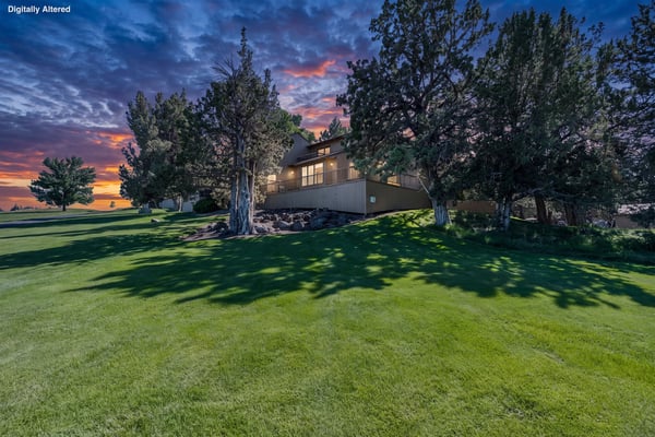 Property nestled among mature trees with stunning sunset skies and manicured lawns, offering a peaceful retreat setting in a natural landscape.