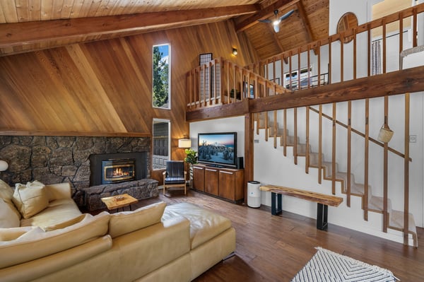 Sink into plush seating by the stone fireplace while warm wood beams frame your mountain retreat. The open loft design invites you to unwind with cozy ambiance and rustic elegance.