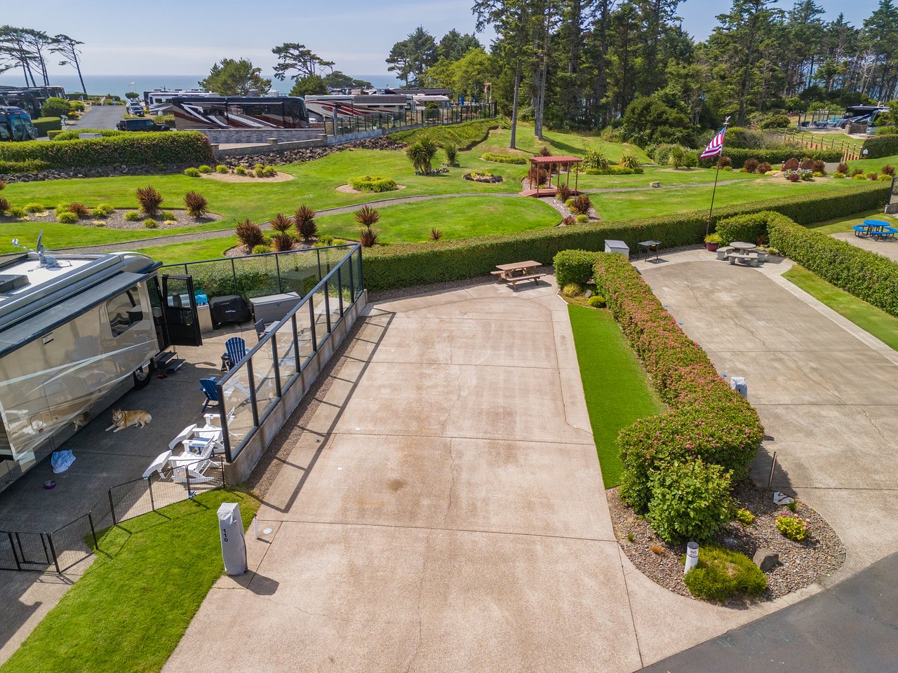 Aerial view of the property grounds featuring well-maintained lawns, picnic areas, and RV parking spaces with coastal access, surrounded by mature trees and landscaped hedges.