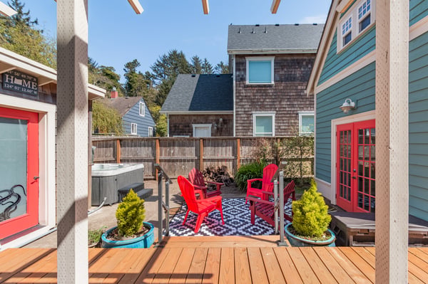 Your private deck awaits with vibrant red chairs, hot tub, and charming coastal views—perfect for morning coffee or evening relaxation.