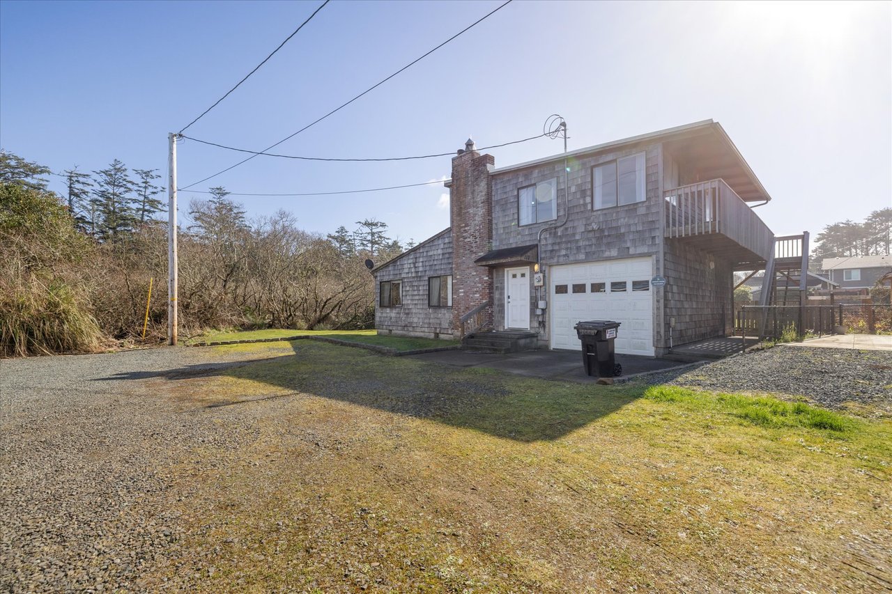 Charming shingled coastal home with private parking and outdoor deck, nestled among mature trees in a peaceful neighborhood setting.