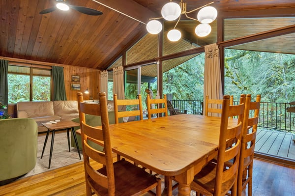 Gather around the rustic dining table beneath vaulted wood ceilings while soaking in forest views through floor-to-ceiling windows. Your cozy living space blends natural warmth with modern comfort.