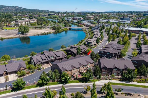 Aerial view of the property showcasing its waterfront location along the Deschutes River, surrounded by green spaces, residential neighborhoods, and mountain vistas—part of the scenic Bend, Oregon area.