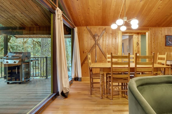 Step into your cozy, wood-paneled retreat where warm lighting and rustic charm create the perfect ambiance for gathering around the dining table or grilling on your private deck surrounded by peaceful forest views.