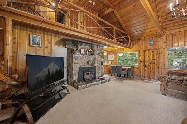 Relax in your cozy mountain retreat with exposed wood beams, stone fireplace, and spacious loft overlooking serene forest views.