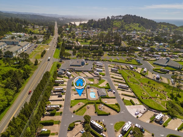 Aerial view of a coastal vacation property surrounded by forested hills, residential neighborhoods, and convenient highway access to nearby amenities and beaches.