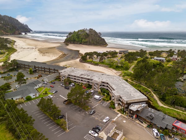 Beachfront property situated along pristine coastline with ocean views, sandy shores, and forested hillsides marking the arrival point for coastal getaways.