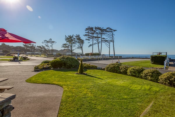 Coastal property grounds feature manicured gardens, mature trees, and pathways leading to the oceanfront with scenic views.