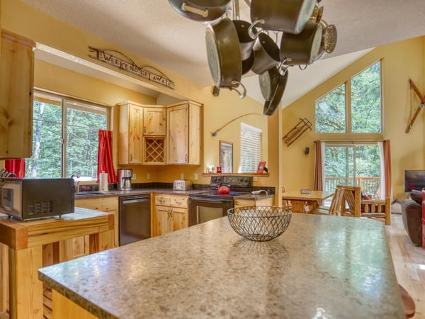Picture yourself preparing meals at the spacious island, with sunlight streaming through tall windows framing peaceful forest views. The open layout flows naturally from cooking to dining, perfect for your mountain getaway.