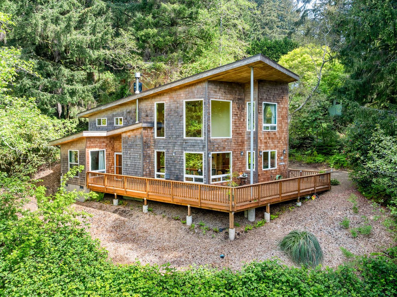 Modern retreat nestled among lush evergreens, featuring a spacious wraparound deck and floor-to-ceiling windows that invite natural light and forest views throughout.