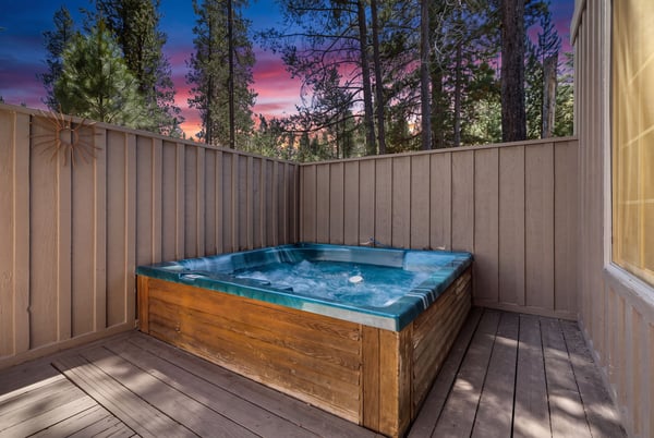 Stunning sunset views paint the sky as the property's private hot tub awaits, surrounded by towering pines in a peaceful, enclosed outdoor space.