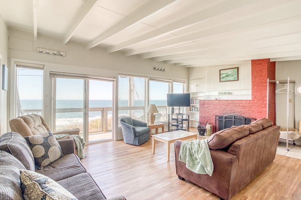 Your oceanfront living room features vaulted ceilings, cozy seating, and panoramic sea views through floor-to-ceiling windows.