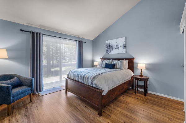 You'll love this peaceful bedroom with soothing blue walls, wood floors, and a cozy queen bed. Natural light flows through balcony doors while ski-themed art hints at nearby slopes.