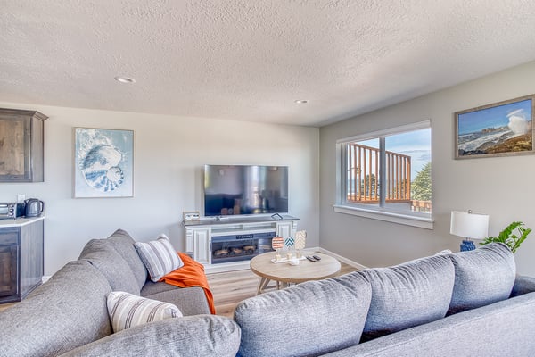 Sink into plush sofas and unwind in your cozy living room, where a fireplace warms the space and natural light streams through windows framing peaceful outdoor views.