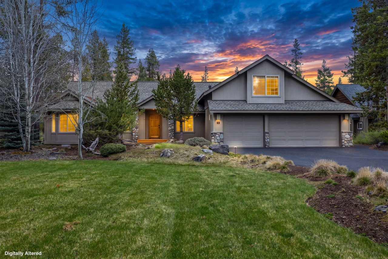 Beautiful mountain home surrounded by tall pines and mature landscaping, featuring warm interior lighting against a stunning sunset backdrop.