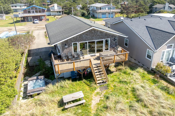 Aerial view showcases the property's spacious wooden deck and coastal neighborhood setting, surrounded by other beach homes and natural landscape.