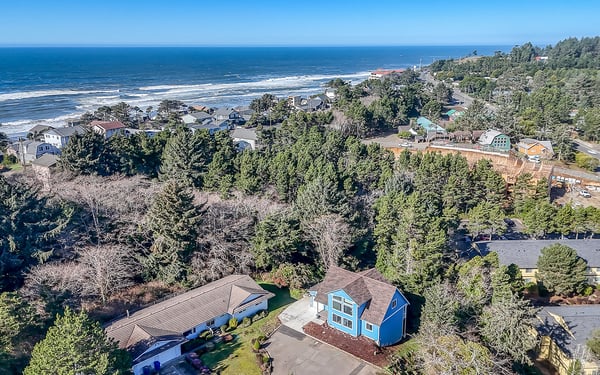 Aerial view of coastal neighborhood with beach access and forested surroundings near the vacation rental property.