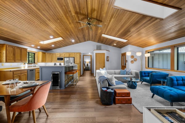 Step into this bright open-concept space where your kitchen, dining, and living areas flow seamlessly together under stunning vaulted wood ceilings with skylights flooding the room with natural light.