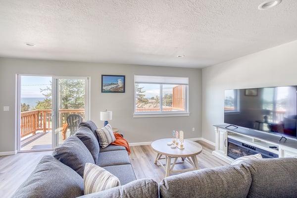 Unwind in your bright, cozy living room with stunning ocean views through large windows and deck access, where coastal breezes and natural light invite you to relax completely.