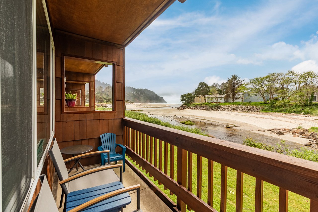 A beachfront retreat frames sweeping coastal vistas, where sandy shores meet forested hills. Two chairs await your morning coffee ritual, just steps from the water's edge.