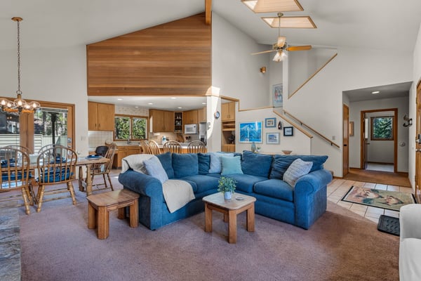 Relax in your spacious living area featuring a plush blue sectional sofa, warm wood accents, and vaulted ceilings with skylights that flood the space with natural light.