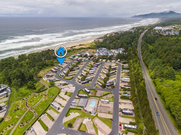 An aerial view of the coastal property nestled between lush forests and pristine beachfront, with mountains rising in the distance along the shoreline.