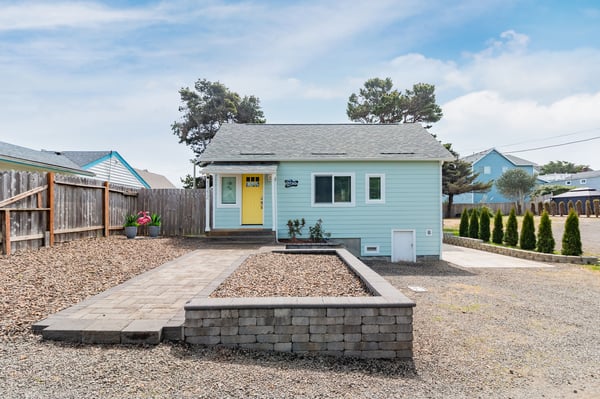 Charming turquoise cottage with sunny yellow door welcomes guests to a peaceful coastal neighborhood retreat.