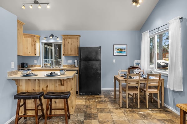 Step into your open kitchen and dining area, where warm wood tones meet soothing blue walls. Gather around the breakfast bar or dining table as natural light streams through white curtains, creating the perfect backdrop for memorable meals together.