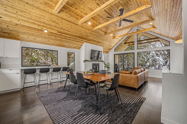 Relax under soaring wood beams in this stunning open-plan retreat, where floor-to-ceiling windows frame snowy forest views while you dine and unwind.