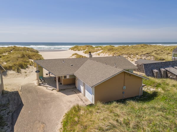 A secluded beachfront property nestled among coastal dunes, offering direct access to pristine sands and ocean surf under clear blue skies.