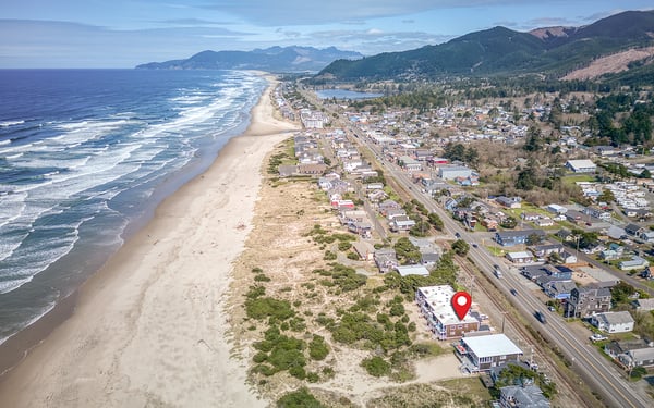 Stunning coastal town setting with pristine beaches stretching along the Pacific shoreline, surrounded by forested mountains.