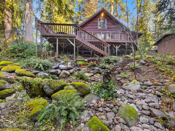 Charming log cabin retreat nestled among towering evergreens with a peaceful moss-covered stone creek meandering through the landscaped grounds.