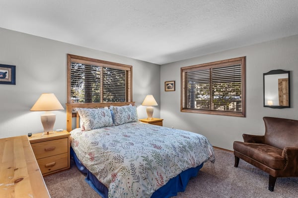 Main Floor Bedroom 1 Unwind in your peaceful bedroom featuring a comfortable queen bed, warm wood furnishings, and natural light streaming through windows.