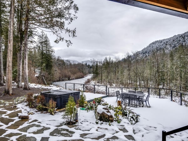 Cozy up in your hot tub while snow blankets the deck, offering breathtaking mountain and river views from your private winter retreat.