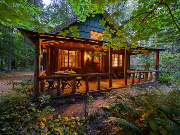 Escape to this enchanting forest cabin where warm lights and wrap-around deck create the perfect woodland retreat sanctuary.